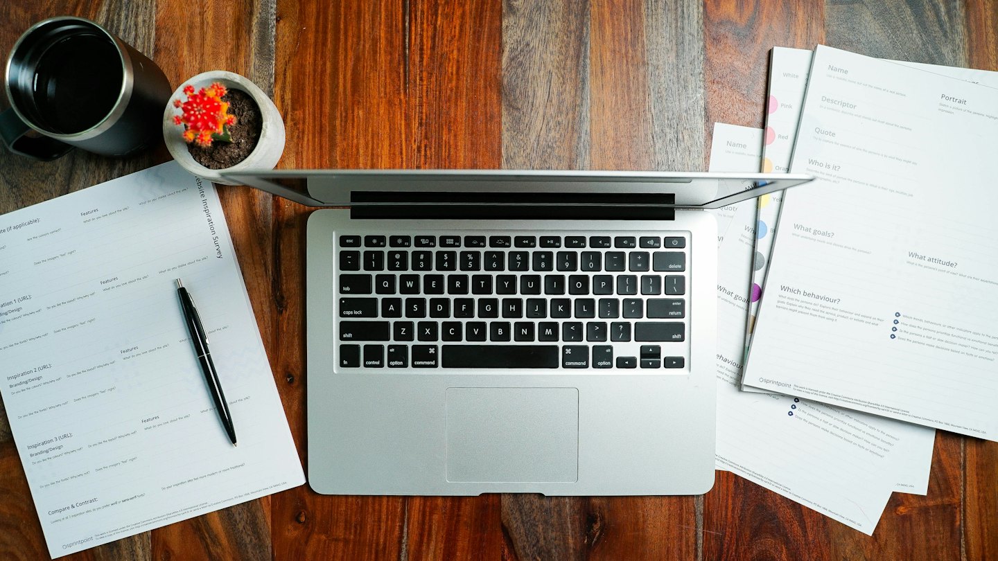 Laptop, survey documents, and pen on a wooden desk.